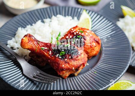 Cosce di pollo speziate in salsa teriyaki o salsa al barbecue con riso in un piatto grigio. Foto Stock