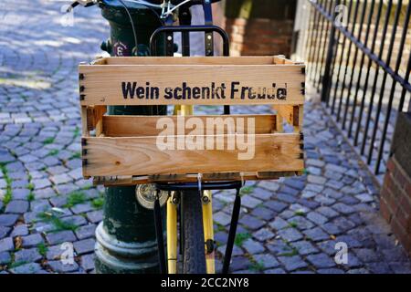 Una bicicletta con cesto di legno che dice 'Wein schenkt Freude' / 'il vino dà piacere' visto in un bel vicolo vecchio con ciottoli nel centro storico di Düsseldorf. Foto Stock