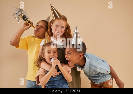 Ritratto in vita di diversi gruppi di bambini che indossano la festa i cappelli gridano al microfono mentre si levano in piedi contro lo sfondo normale dentro studio Foto Stock