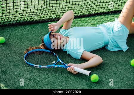 Giovane ragazza sdraiata sulla schiena sul campo da tennis, guardando la macchina fotografica. Angolo alto Foto Stock