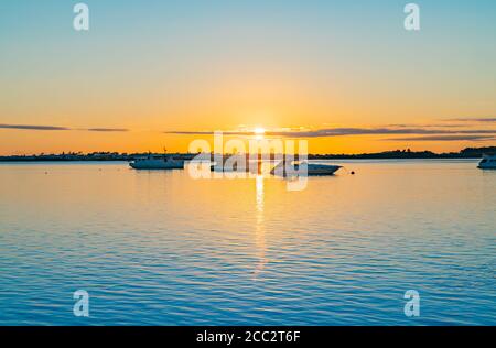 Tre barche ormeggiate vicino all'orizzonte all'alba sull'acqua blu Del porto di Tauranga con intensa luce dorata di sole orizzonte Foto Stock