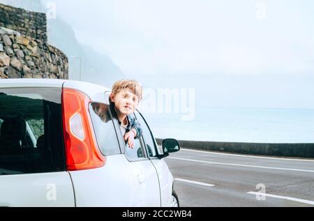 Ragazzo adolescente capelli biondi guardando fuori dalla porta posteriore passangers di classe economica auto e smiling.Rental auto e viaggiare da auto concept immagine. Foto Stock