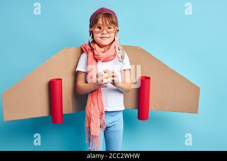 Giocoso ragazzo che indossa tuta pilota, casco e platano di cartone isolato su sfondo blu Foto Stock