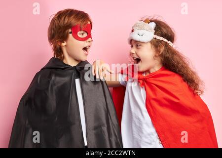 Due bambini carini che indossano abiti da eroe e maschere si trovano isolati su sfondo rosa, la togetherness, la squadra dei bambini. Concetto Suprehero Foto Stock