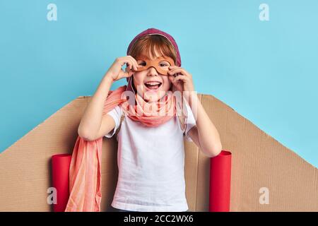 Giocoso ragazzo che indossa tuta pilota, casco e platano di cartone isolato su sfondo blu Foto Stock