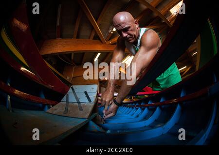 VENEZIA, ITALIA - 18 LUGLIO 2017: Un artigiano veneziano costruisce una barca di legno blu nel suo cantiere Foto Stock