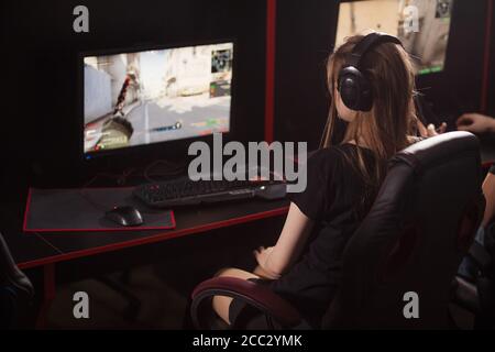 Sul retro di una giovane donna che indossa le cuffie a lungo I capelli biondi sta partecipando al torneo in linea dei cyber giochi dentro Internet Cafe Foto Stock