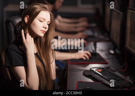 Bella donna gamer indossare cuffie, giocare in videogioco online con un'altra gente seduto in fila accanto al club. ESport Cyber Games Internet Foto Stock