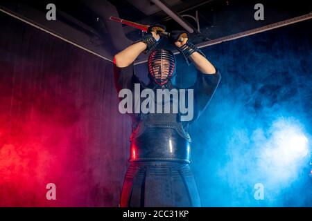Combattente caucasico maschile kendo in stile tradizionale giapponese di abbigliamento, armatura protettiva, utilizzando shinai. Pratica lotta isolato sopra camera fumosa Foto Stock