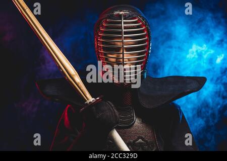 ritratto del combattente del kendo in uniforme e casco protettivo. guerriero di combattimento che tiene lo shinai in mano spada di bambù isolata sullo spazio fumoso Foto Stock