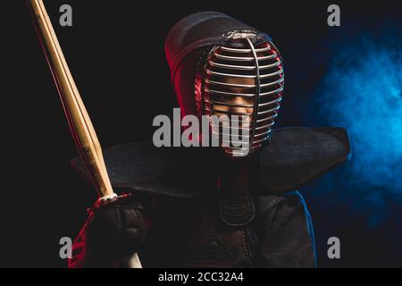 Ritratto di giovane combattente Kendo con spada di bambù shinai isolato sullo spazio fumoso. Tradizione armatura kendo, samurai Foto Stock