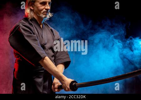 Combattente caucasico maschile kendo in stile tradizionale giapponese di abbigliamento, armatura protettiva, utilizzando shinai. Pratica lotta isolato sopra camera fumosa Foto Stock
