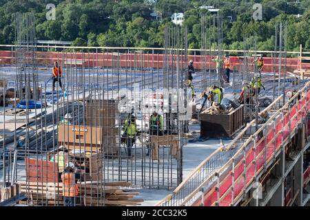 L'equipaggio di costruzione che indossa attrezzatura di sicurezza completa e rivestimenti del viso lavora su forme di costruzione per colonne di cemento per garage di alta torre che sale nel quartiere di Rainey Street vicino al centro di Austin Texas. Foto Stock