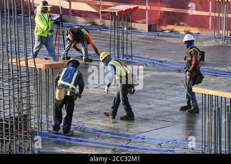 L'equipaggio di costruzione che indossa attrezzatura di sicurezza completa e rivestimenti del viso lavora su forme di costruzione per colonne di cemento per garage di alta torre che sale nel quartiere di Rainey Street vicino al centro di Austin Texas. Foto Stock