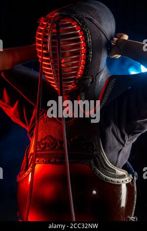 Ritratto di giovane combattente Kendo con spada di bambù shinai isolato sullo spazio fumoso. Tradizione armatura kendo, samurai Foto Stock