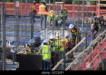 L'equipaggio di costruzione che indossa attrezzatura di sicurezza completa e rivestimenti del viso lavora su forme di costruzione per colonne di cemento per garage di alta torre che sale nel quartiere di Rainey Street vicino al centro di Austin Texas. Foto Stock