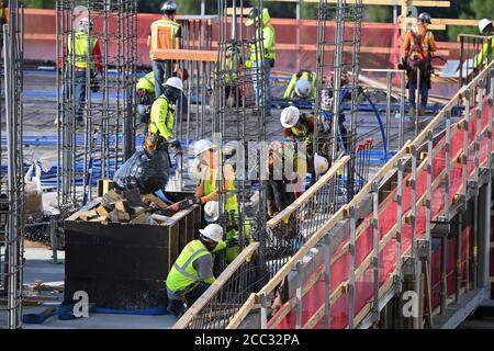 L'equipaggio di costruzione che indossa attrezzatura di sicurezza completa e rivestimenti del viso lavora su forme di costruzione per colonne di cemento per garage di alta torre che sale nel quartiere di Rainey Street vicino al centro di Austin Texas. Foto Stock