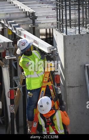 I lavoratori edili che indossano attrezzature di sicurezza e rivestimenti per il viso si trovano sul posto di lavoro del parcheggio nel quartiere di Rainey Street, vicino al centro di Austin, Texas. Foto Stock