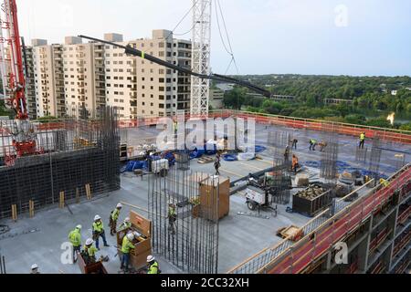 L'equipaggio di costruzione che indossa attrezzatura di sicurezza completa e rivestimenti del viso lavora su forme di costruzione per colonne di cemento per garage di alta torre che sale nel quartiere di Rainey Street vicino al centro di Austin Texas. Foto Stock