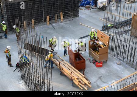 L'equipaggio di costruzione che indossa attrezzatura di sicurezza completa e rivestimenti del viso lavora su forme di costruzione per colonne di cemento per garage di alta torre che sale nel quartiere di Rainey Street vicino al centro di Austin Texas. Foto Stock