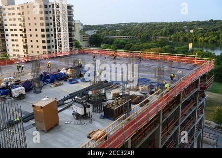 L'equipaggio di costruzione che indossa attrezzatura di sicurezza completa e rivestimenti del viso lavora su forme di costruzione per colonne di cemento per garage di alta torre che sale nel quartiere di Rainey Street vicino al centro di Austin Texas. Foto Stock