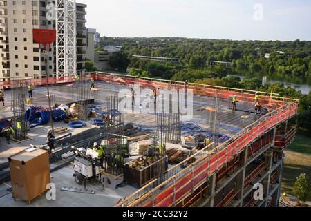 L'equipaggio di costruzione che indossa attrezzatura di sicurezza completa e rivestimenti del viso lavora su forme di costruzione per colonne di cemento per garage di alta torre che sale nel quartiere di Rainey Street vicino al centro di Austin Texas. Foto Stock