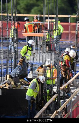 L'equipaggio di costruzione che indossa attrezzatura di sicurezza completa e rivestimenti del viso lavora su forme di costruzione per colonne di cemento per garage di alta torre che sale nel quartiere di Rainey Street vicino al centro di Austin Texas. Foto Stock