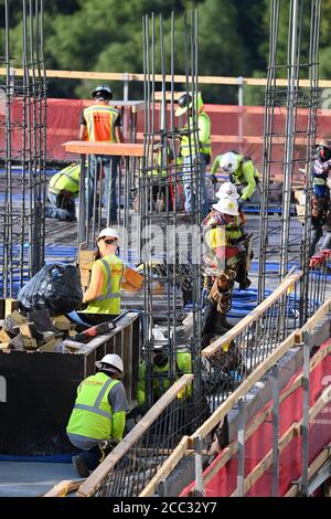 L'equipaggio di costruzione che indossa attrezzatura di sicurezza completa e rivestimenti del viso lavora su forme di costruzione per colonne di cemento per garage di alta torre che sale nel quartiere di Rainey Street vicino al centro di Austin Texas. Foto Stock