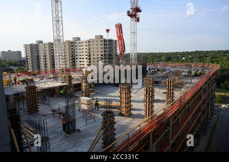 L'equipaggio di costruzione che indossa attrezzatura di sicurezza completa e rivestimenti del viso lavora su forme di costruzione per colonne di cemento per garage di alta torre che sale nel quartiere di Rainey Street vicino al centro di Austin Texas. Foto Stock