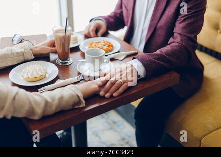 uomo anziano che tiene la mano della moglie mentre si siede nel caffè. uomo che sostiene la sua donna in una situazione difficile, coppia che supera i problemi della famiglia Foto Stock