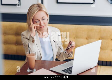 donna stanca che strofina gli occhi dopo aver lavorato sul laptop. primo piano foto. stanchezza, donna assonnata seduta al tavolo e utilizzando il computer Foto Stock