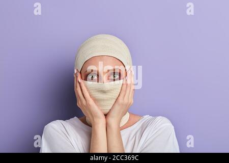 ragazza spaventata che tocca la guancia dopo un intervento chirurgico di plastica. primo piano ritratto, isolato sfondo blu, studio shot. copia spazio Foto Stock