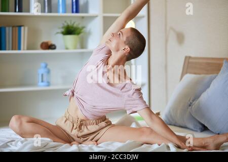 Donna caucasica a letto pratica esercizi di yoga, sfondo camera bianca. Mani sollevate. Foto Stock