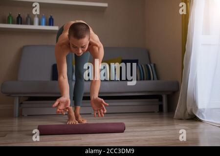 Attraente donna di yoga che rotola il suo tappetino lilla dopo la pratica di yoga a casa. Vita sana, sport, hobby Foto Stock