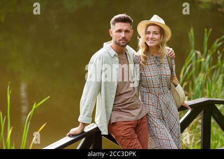 Ritratto di una romantica coppia di adulti guardando la macchina fotografica mentre ci si trova vicino al lago all'aperto in un paesaggio rustico, spazio copia Foto Stock