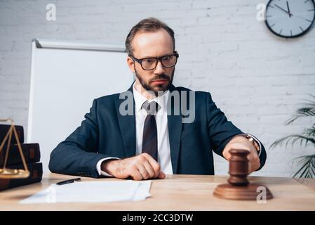 fuoco selettivo del giudice bearded nei vetri che guardano il gavel vicino a carte sul tavolo Foto Stock