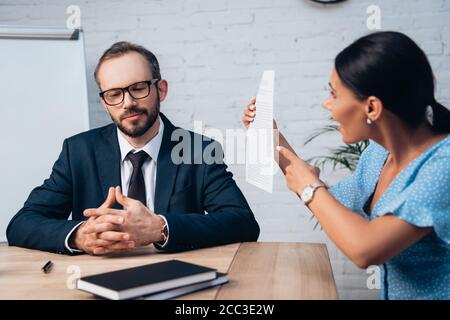 fuoco selettivo di avvocato bearded in occhiali seduti con clenched mani vicino al cliente che punta con il dito al contratto in ufficio Foto Stock