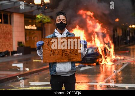 Seattle, USA 30 maggio 2020: Un attivista con un cartello NO JUSTICE NO PEACE, mentre un'auto della polizia brucia sullo sfondo a Westlake. Foto Stock