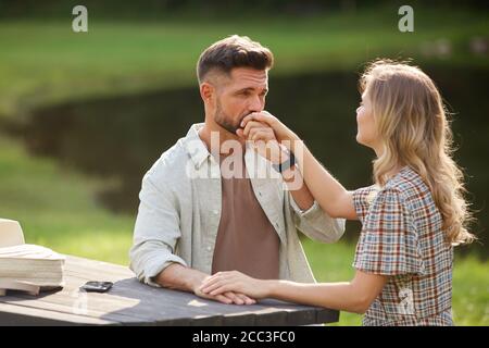 Ritratto di bell'uomo adulto baciando mano di bella donna mentre godendo la data romantica all'aperto vicino al lago, copia spazio Foto Stock