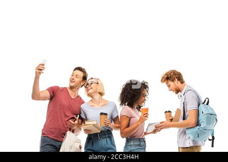 Studenti multiculturali con caffè per andare a prendere selfie e tenere libri isolati su bianco Foto Stock