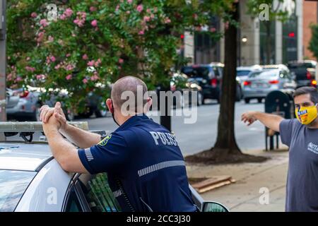 Frederick, MD, USA 08/14/2020: Un giovane poliziotto maschio caucasico che indossa una maschera sta rispondendo ad una domanda posta da una persona che indossa anche Foto Stock