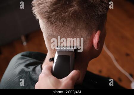 taglio di capelli da uomo, il maestro taglia il ragazzo con un regolacapelli, un apparecchio per capelli. Foto Stock