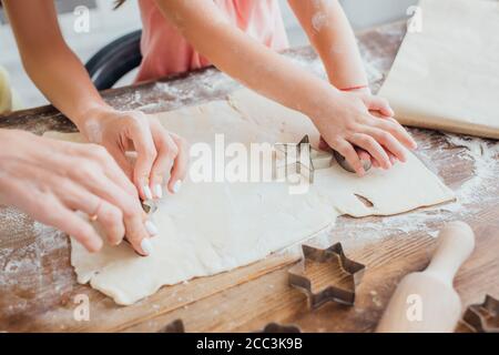 vista parziale di donne e bambini che tagliano i biscotti pasta arrotolata vicino a stampi a forma di stella Foto Stock