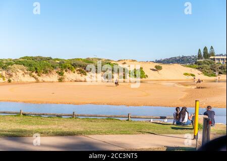 Persone che riposano su un'area erbosa nei laghi di Narrabeen, spiagge del Nord in un pomeriggio di sole autunno Foto Stock