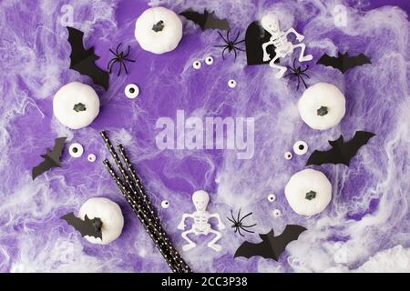 Decorazioni di Halloween. Zucche bianche decorative, pipistrelli, occhi, scheletri, cannucce per cocktail su sfondo viola. Concetto di festa di Halloween. FLA Foto Stock