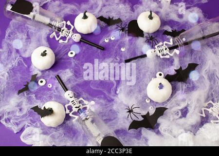 Buon concetto di vacanza di Halloween. Decorazioni spaventose, ragnatele, zucche, pipistrelli, bottiglie per cocktail e paillette su sfondo viola. Messaggio di saluto della festa Foto Stock