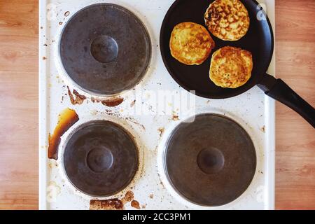 stufa sporca con macchie di cibo bruciato e grasso, padella con frittelle sulla parte superiore Foto Stock