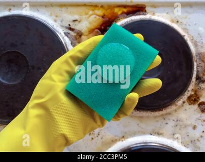 tenere la spugna per guanti per uso domestico con il liquido detergente sopra stufa sporca Foto Stock
