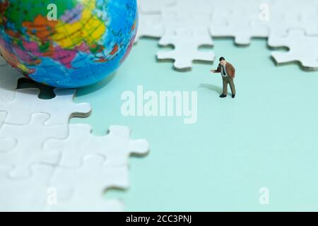 Business strategy Conceptual photo - uomo d'affari in miniatura che punta su vuoto puzzle spazio con globo Foto Stock