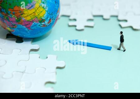 Business strategy Conceptual photo - uomo d'affari in miniatura che cammina nel globo nel mezzo del puzzle Foto Stock